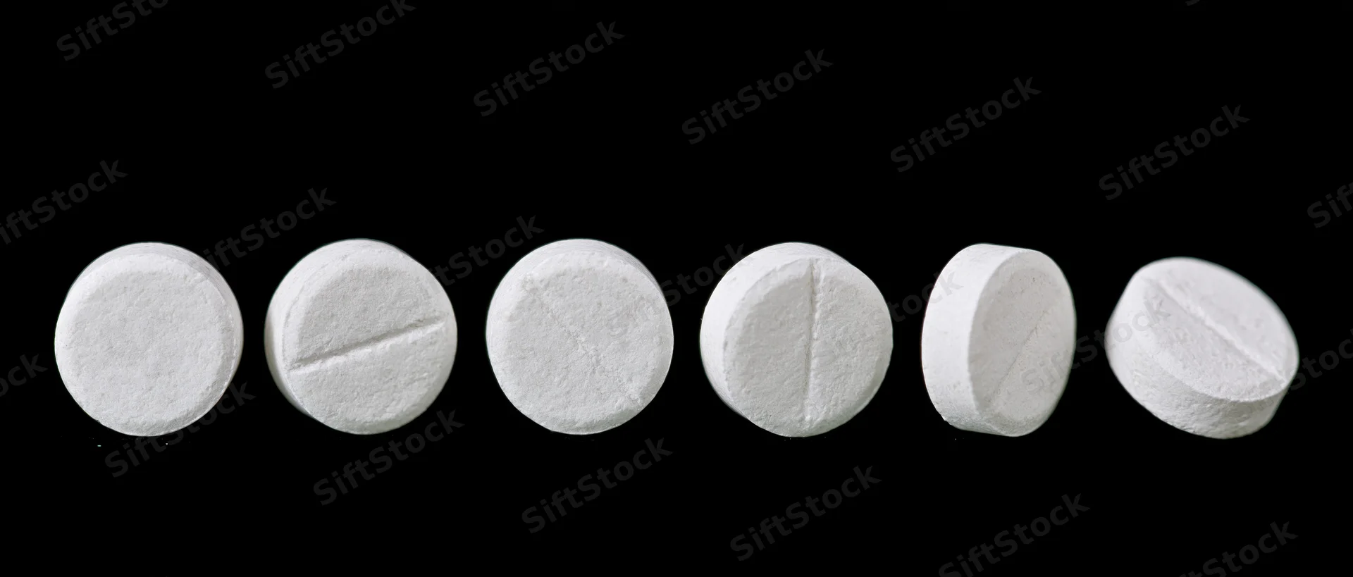 White round pharmaceutical tablets arranged in a row on black background