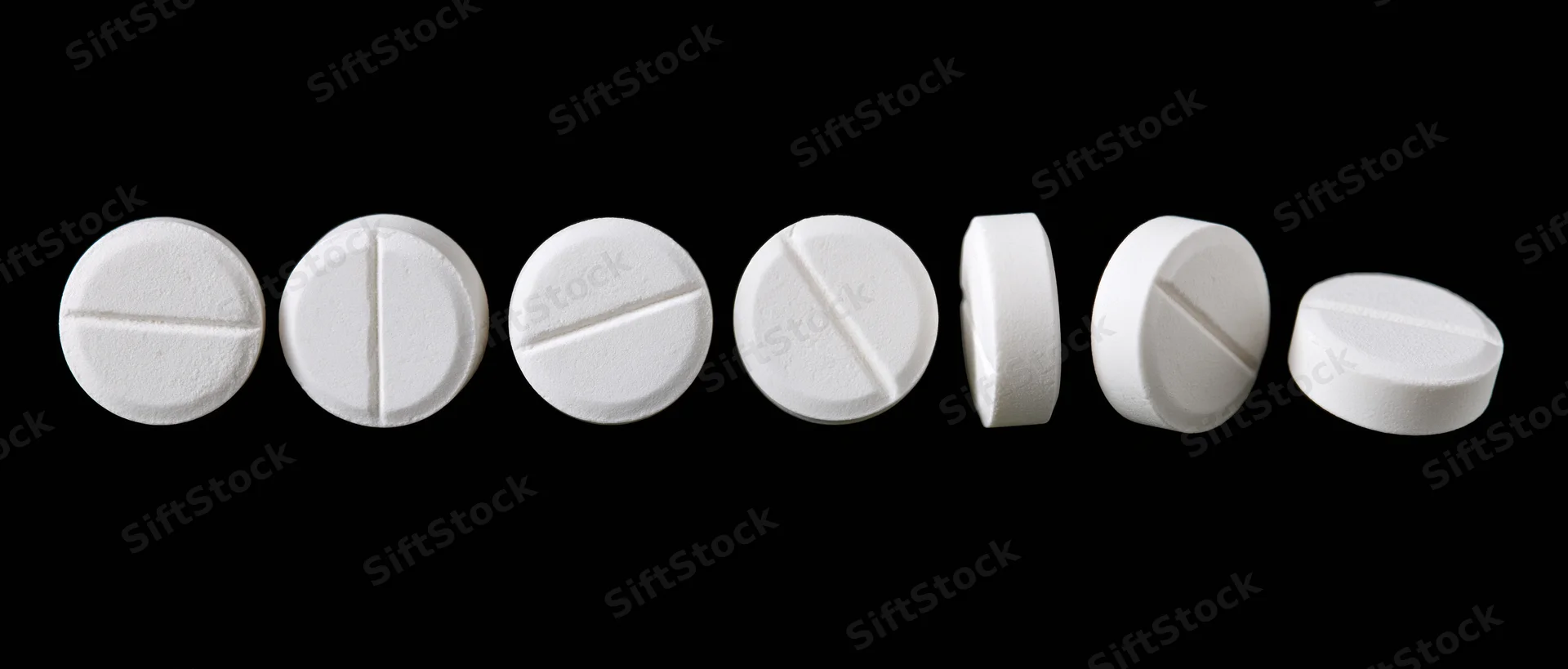 Eight white round pharmaceutical tablets arranged in a horizontal row on a black background