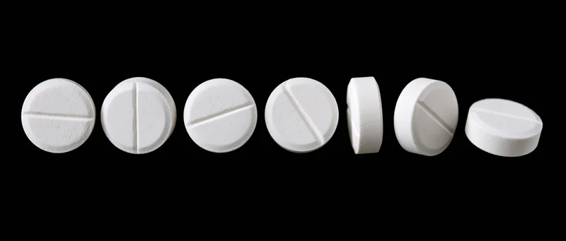 Eight white round pharmaceutical tablets arranged in a horizontal row on a black background