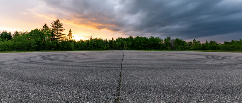 Empty asphalt racing circuit with circular tire skid marks under cloudy sunset sky