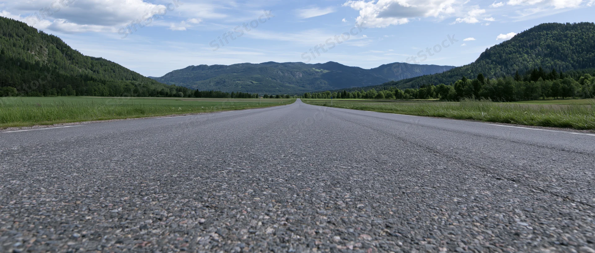 Straight asphalt road stretching toward distant mountains through green valley