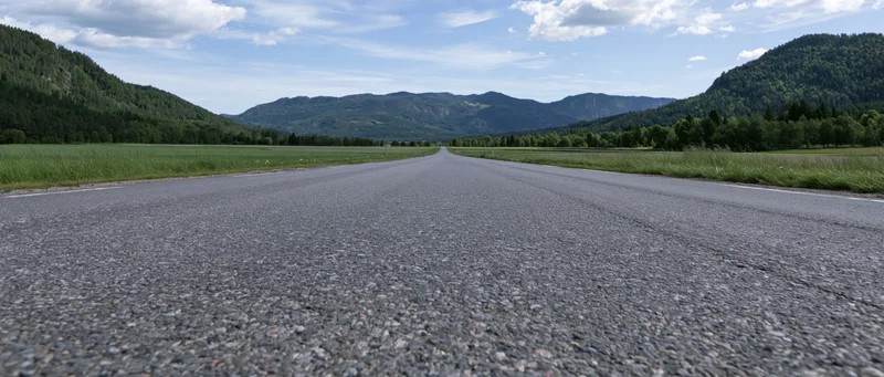 Straight asphalt road stretching toward distant mountains through green valley
