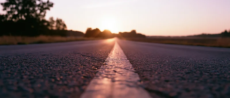 Empty asphalt road stretching toward the horizon at sunset with white line in focus