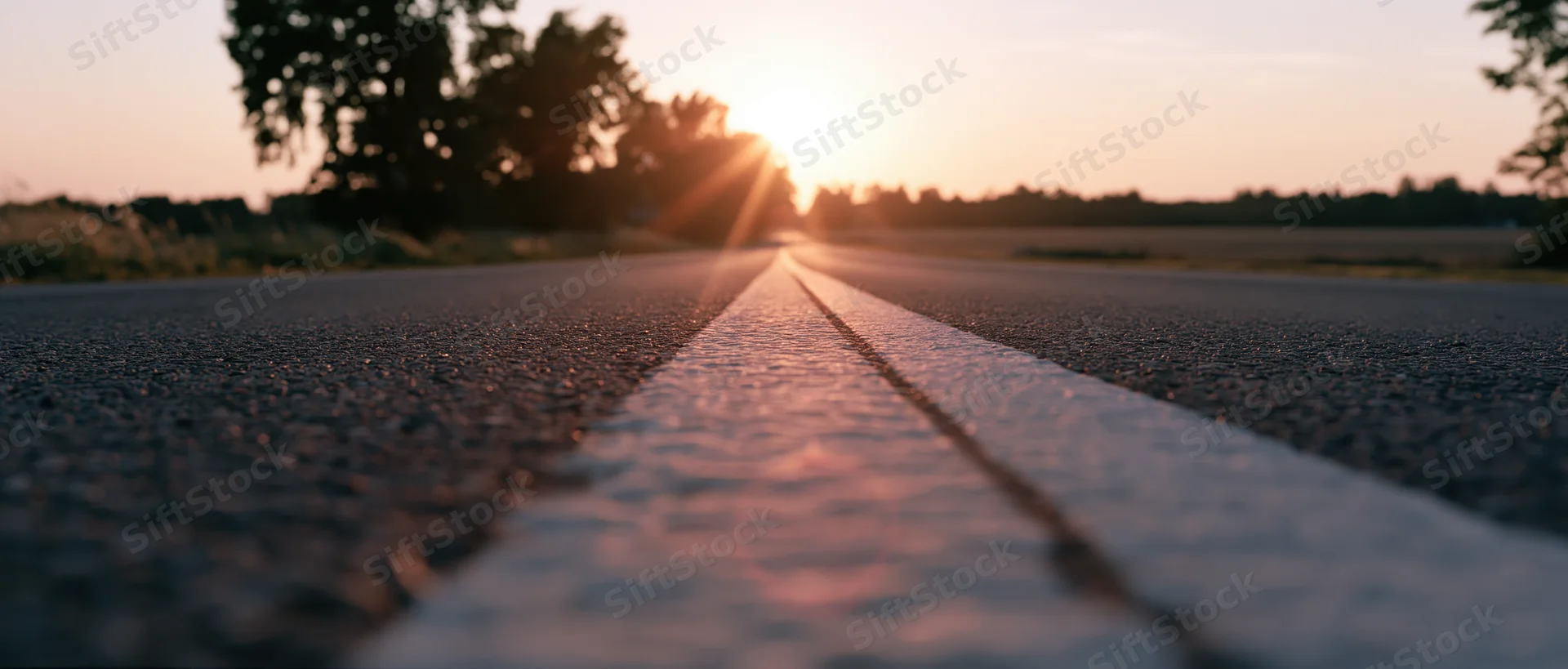 Empty asphalt road stretching toward the horizon at sunset with white line in focus