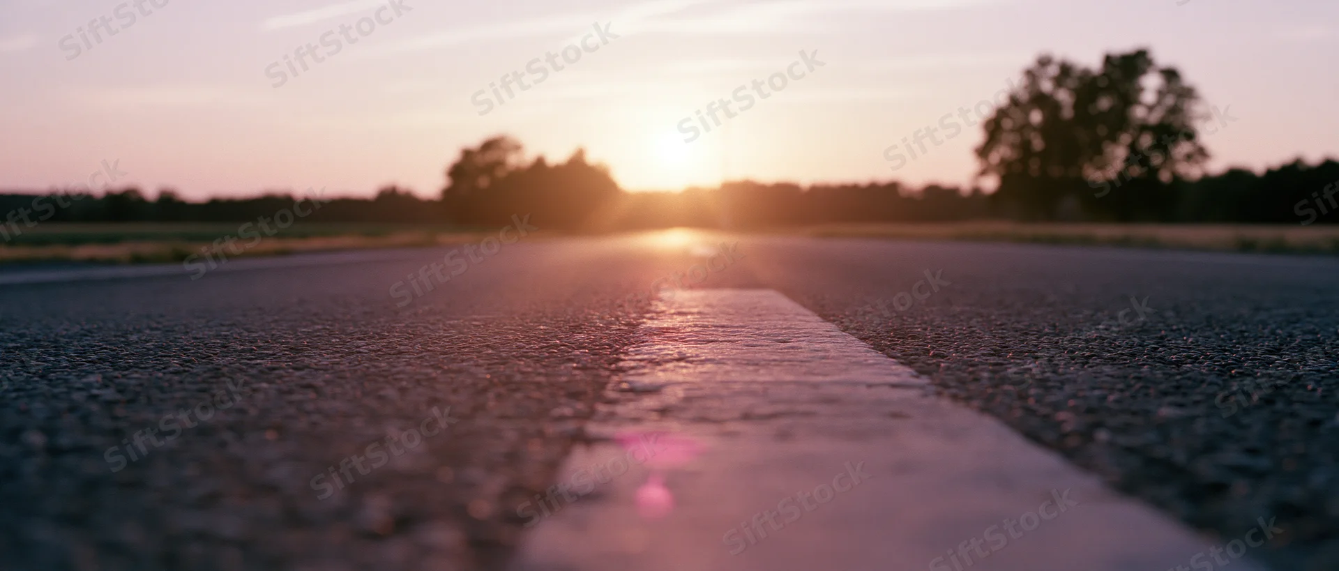 Empty asphalt road stretching toward the horizon at sunset with white line in focus