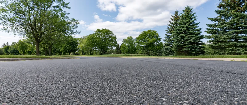 Low-angle view of empty asphalt road stretching toward tree-lined horizon under partly cloudy sky