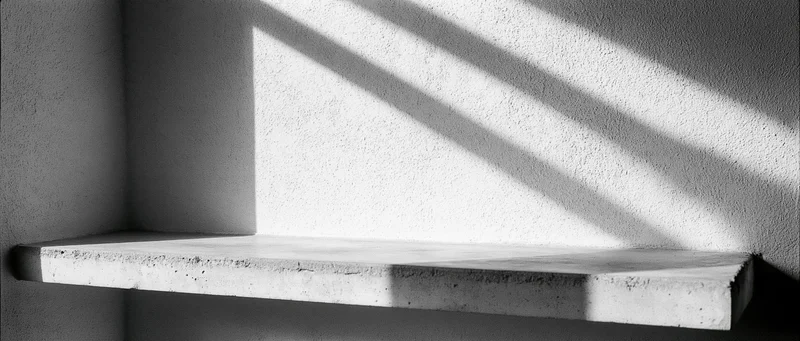 Empty concrete shelf in a corner against a textured plaster wall with diagonal shadows from sunlight
