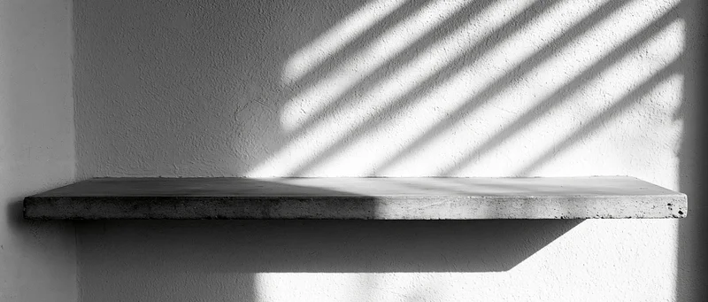 Empty concrete shelf mounted on a textured plaster wall with diagonal sunlight shadows