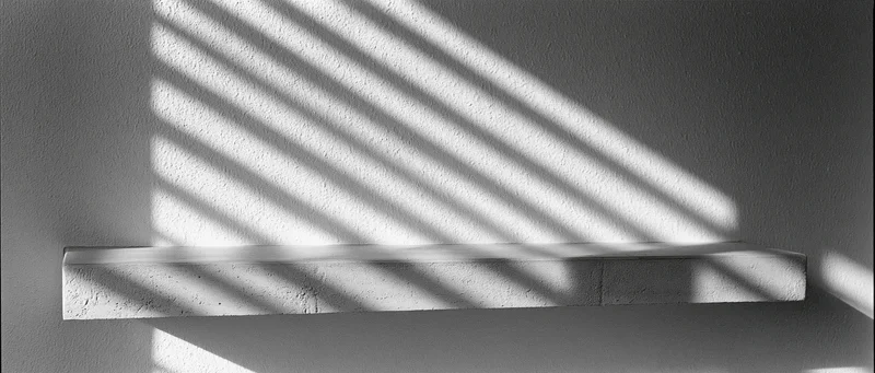 Concrete shelf mounted on textured plaster wall with diagonal sunlight shadows