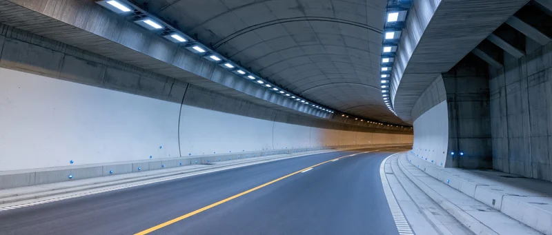 Empty curved highway tunnel interior with concrete walls and overhead lighting