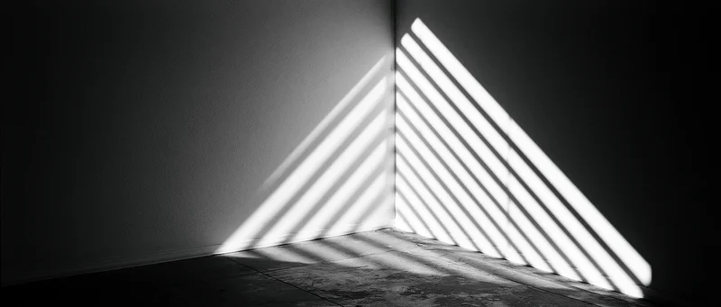 Diagonal light stripes from venetian blind cast on dark room corner wall and floor