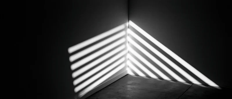 Diagonal light stripes from venetian blinds cast on dark room corner walls and floor