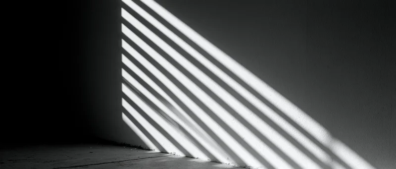 Diagonal light stripes from venetian blind cast on dark wall and floor in empty room corner