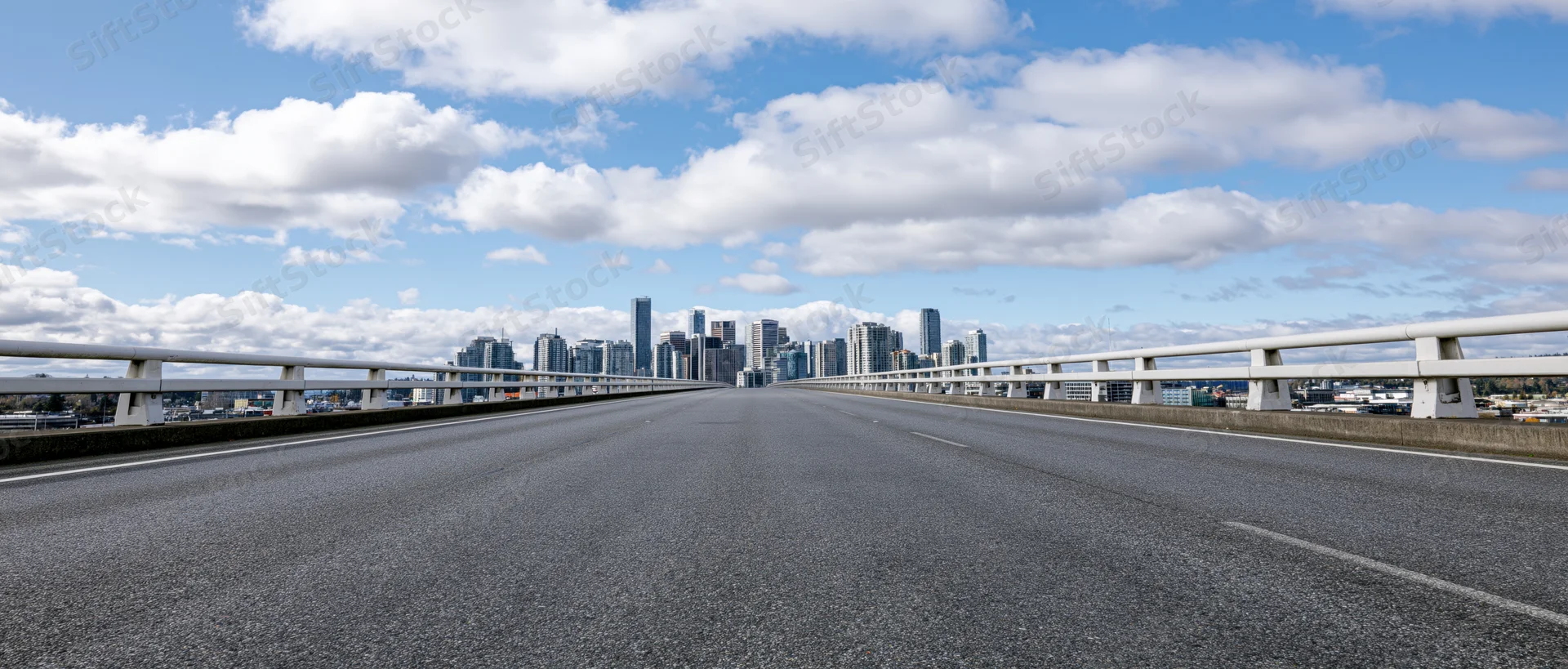 Empty elevated highway overpass with white concrete guardrail leading toward city skyline