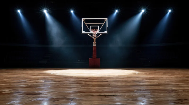 Basketball hoop illuminated by spotlights on an empty indoor court at night