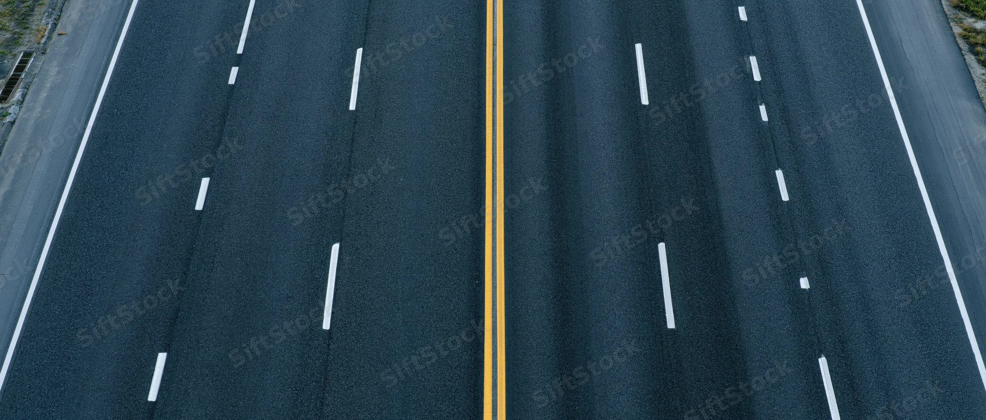 Overhead view of multi-lane asphalt highway with yellow center divider and white lane markings