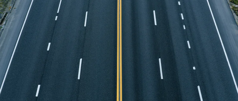 Overhead view of multi-lane asphalt highway with yellow center divider and white lane markings