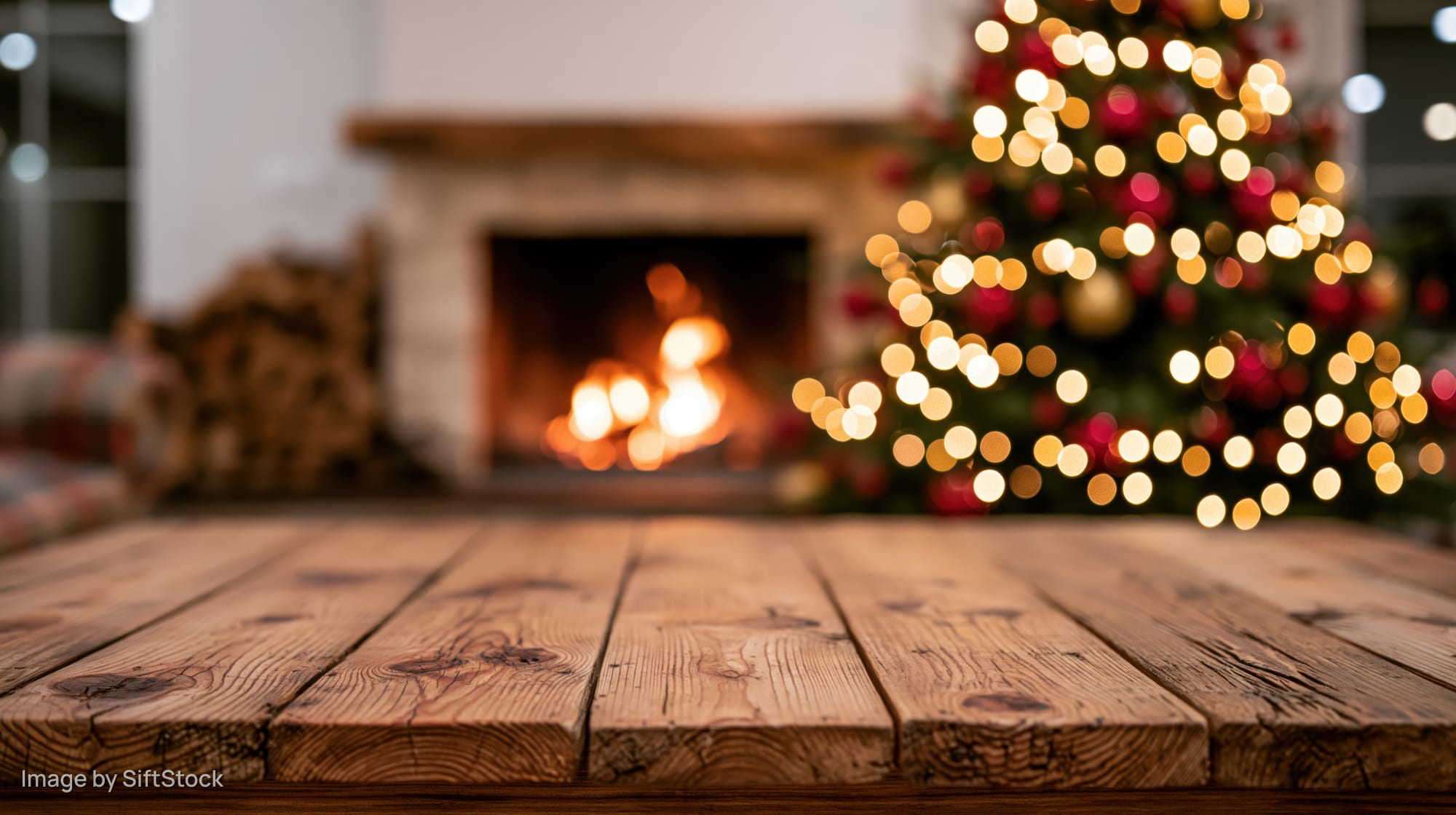 Rustic wooden tabletop in front of a lit fireplace and decorated christmas tree in a cozy living room