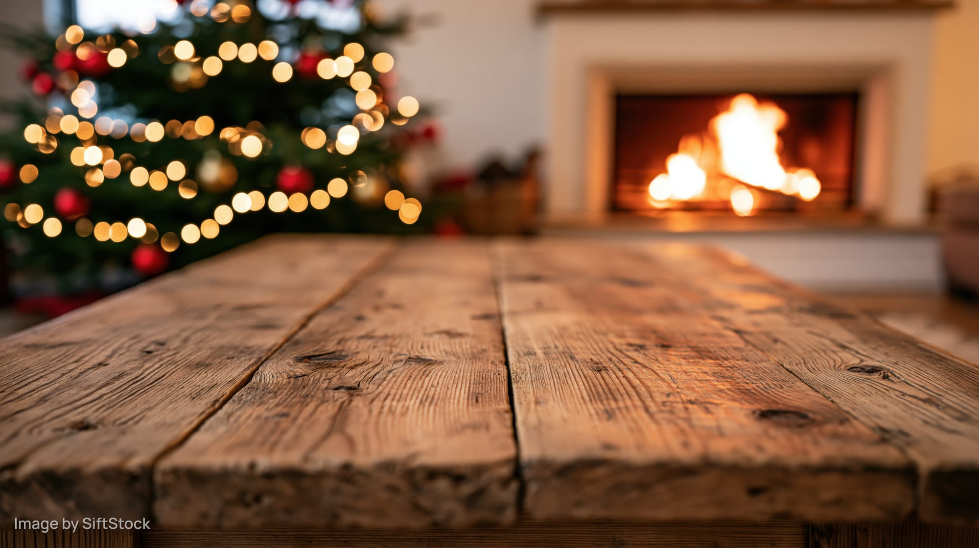 Rustic wooden table in foreground with blurred christmas tree and fireplace in background