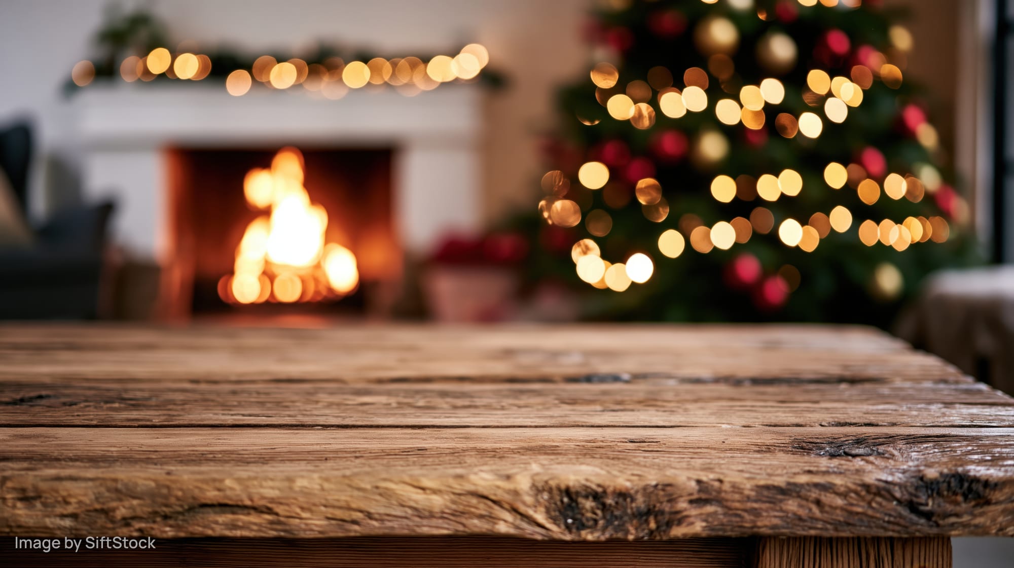 Rustic wooden table in foreground with blurred christmas tree and fireplace in background