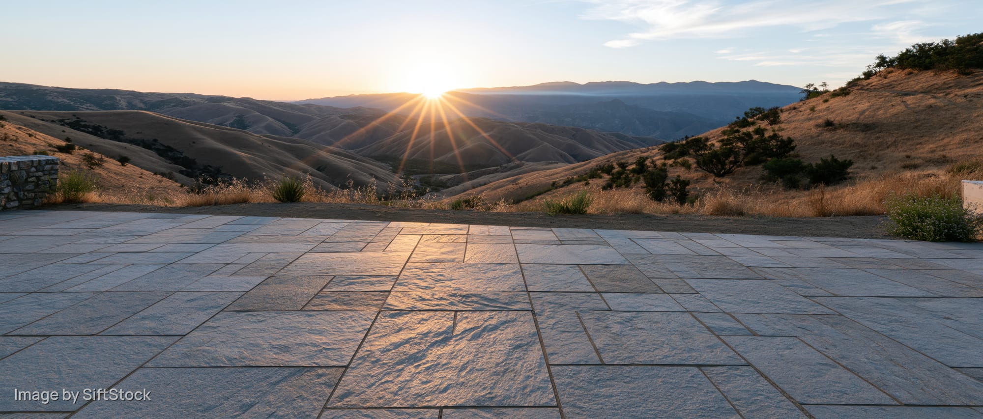 Stone tile plaza floor in foreground with sunset over mountainous landscape