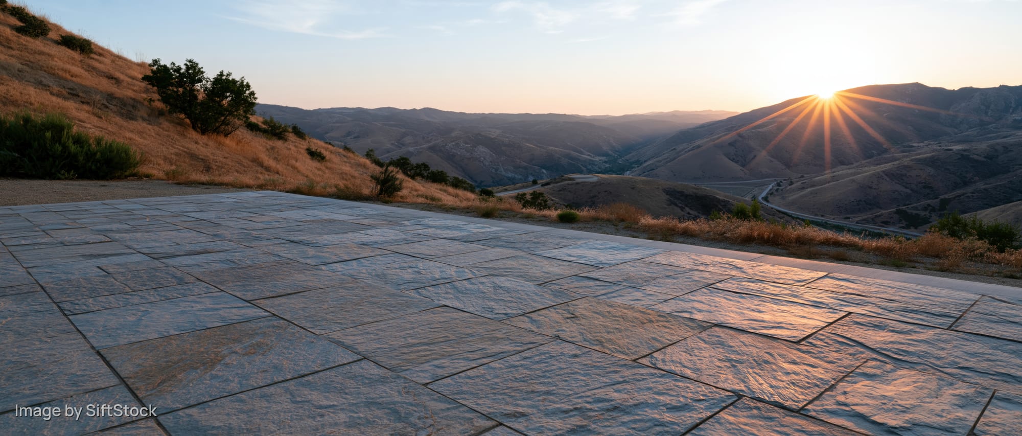 Stone tile plaza floor in foreground with mountain valley and sunset in distance