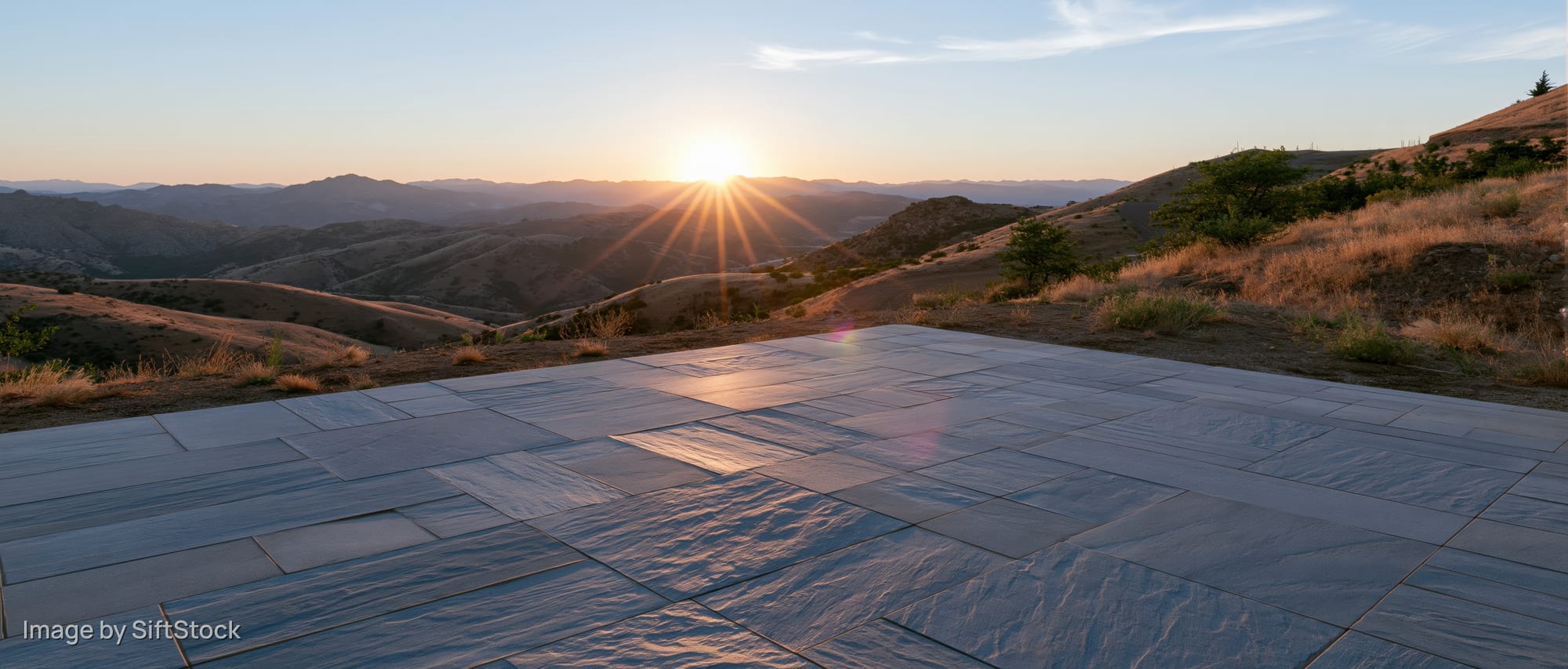 Stone tile plaza floor in a wide outdoor view at sunset with mountains in the background
