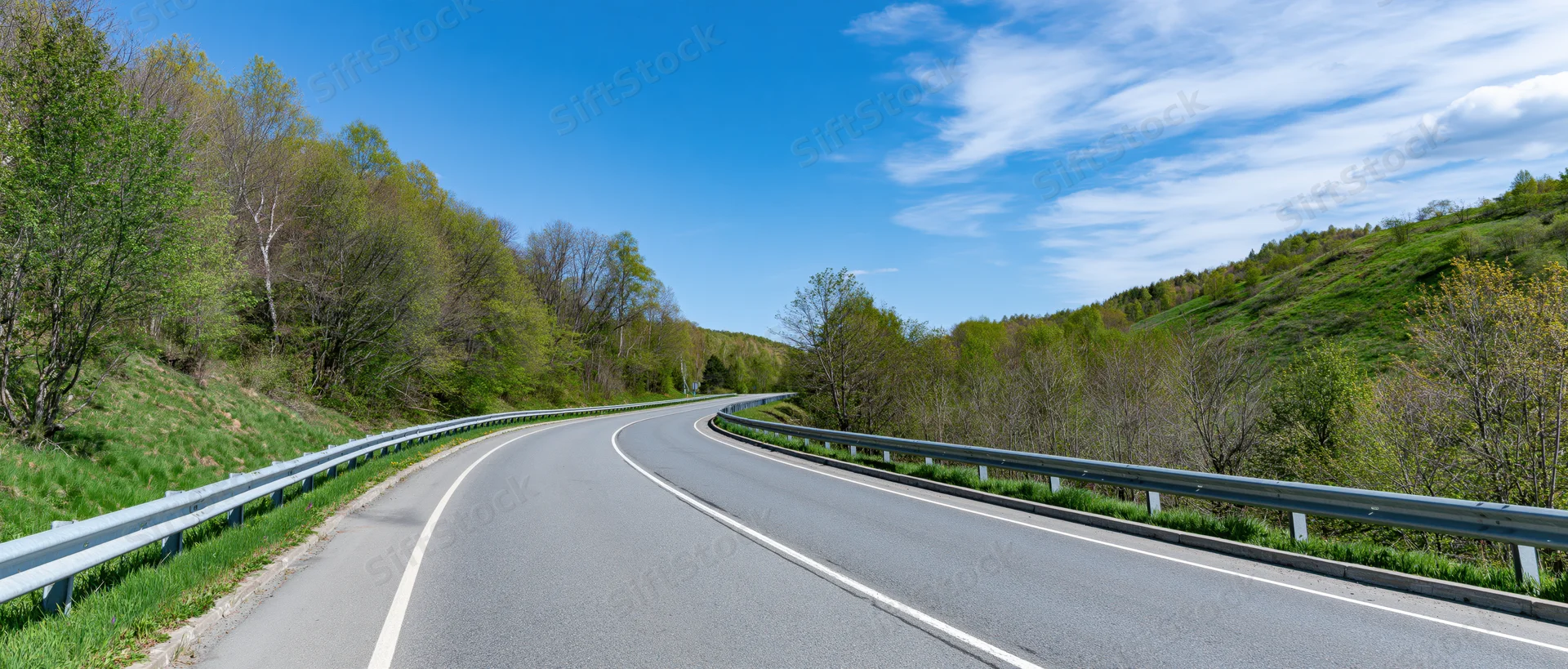Winding asphalt highway curving through green forested hills under blue sky