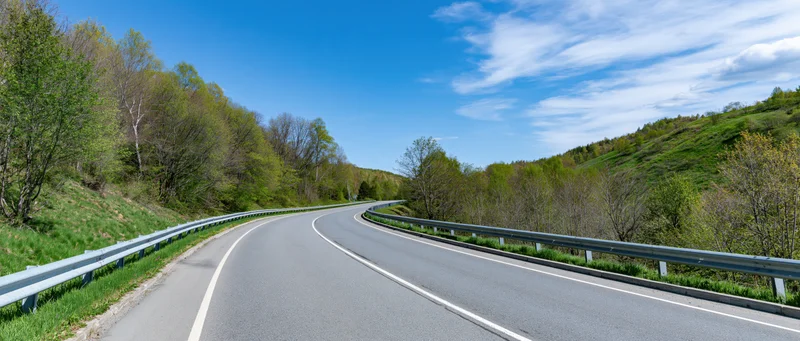 Winding asphalt highway curving through green forested hills under blue sky