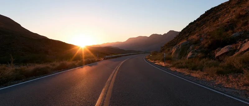 Winding asphalt highway curves through desert mountains at sunset
