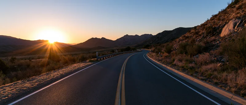Winding asphalt highway curves through desert landscape at sunset
