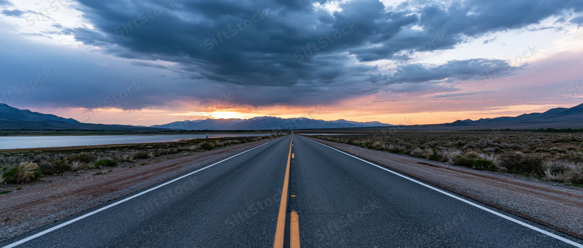 Straight asphalt highway stretching toward distant mountains at sunset over desert landscape
