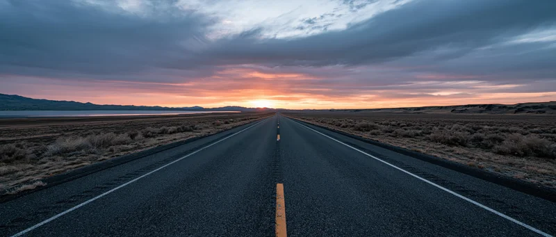 Straight asphalt highway stretching toward sunset over desert landscape