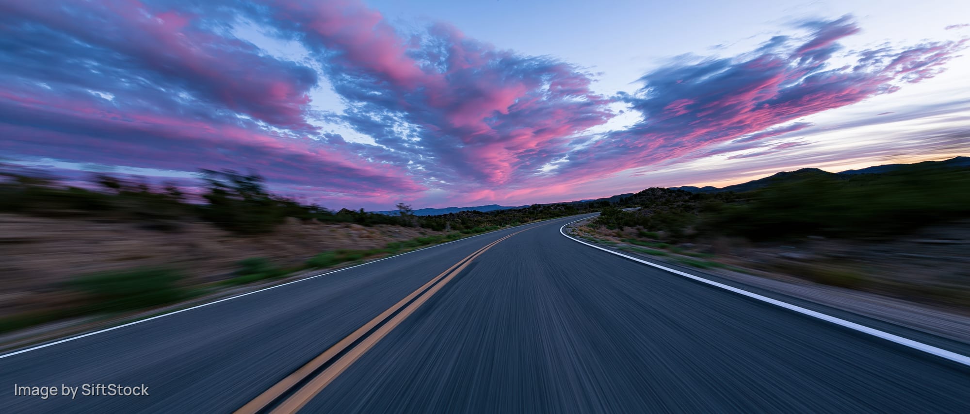 Winding asphalt highway stretching toward the horizon under a pink and purple sunset sky
