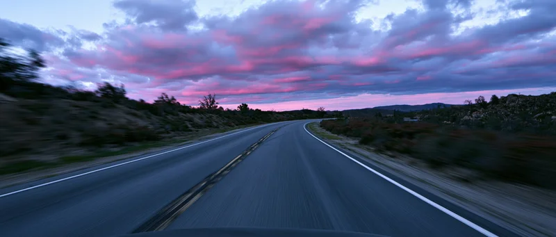 View from car driving on winding asphalt highway toward horizon at twilight