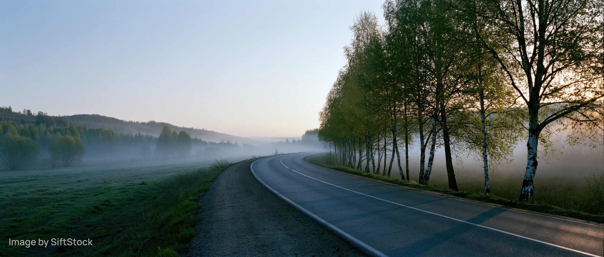 Winding asphalt road curving through foggy rural landscape at dawn