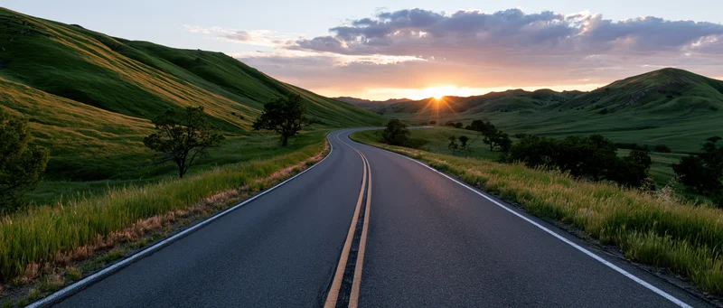 Winding asphalt road through green rolling hills at sunset