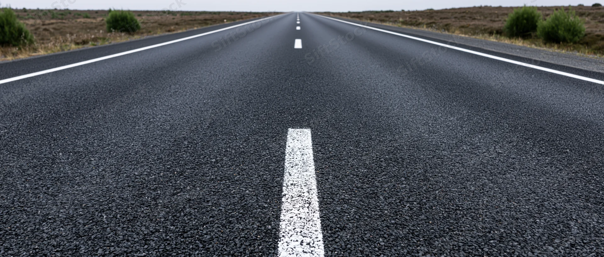Straight asphalt road with white center line stretching to vanishing point in rural landscape