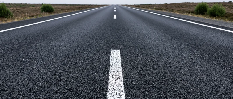 Straight asphalt road with white center line stretching to vanishing point in rural landscape