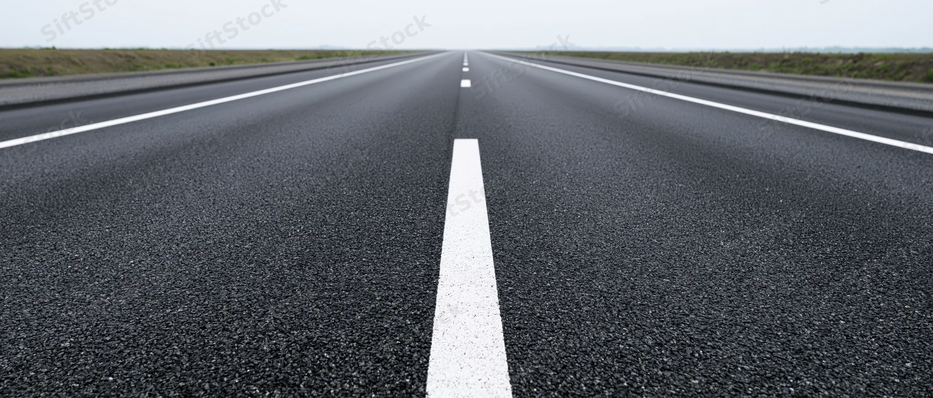 Straight asphalt road with white center line stretching to horizon in rural landscape