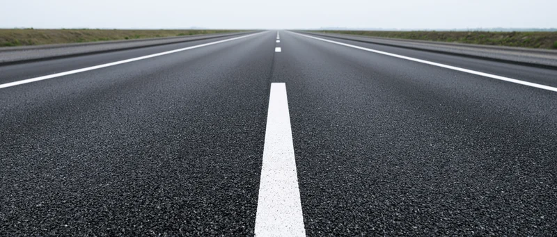 Straight asphalt road with white center line stretching to horizon in rural landscape