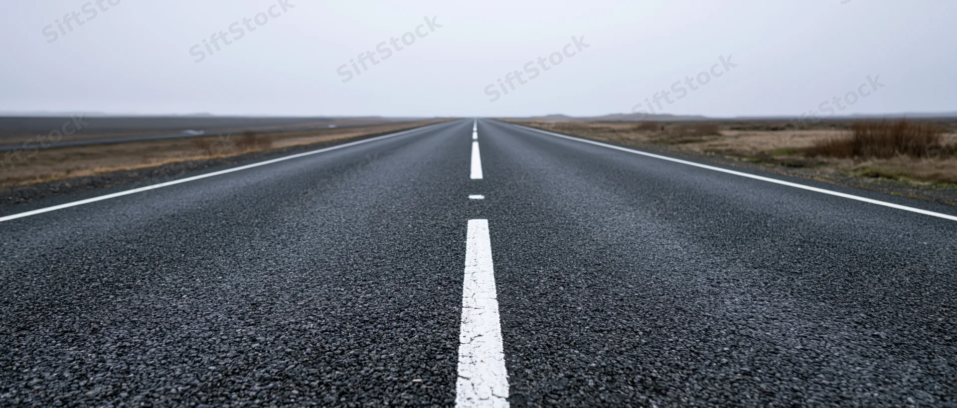 Straight asphalt road stretching to the horizon through open rural landscape