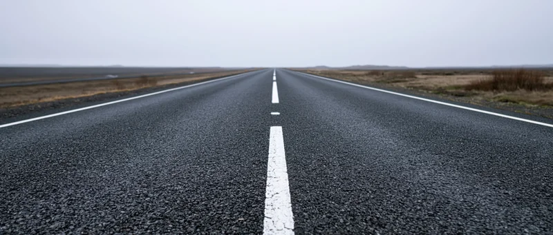Straight asphalt road stretching to the horizon through open rural landscape