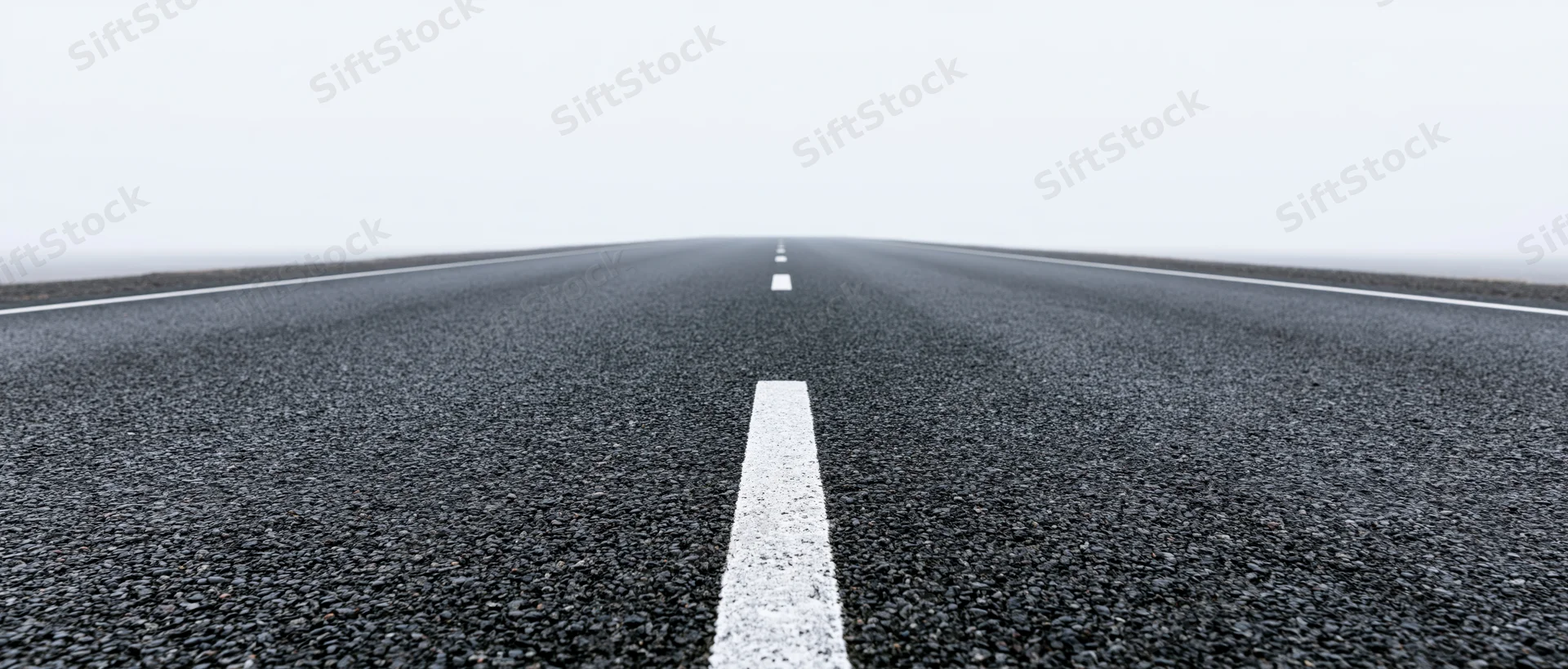 Straight asphalt road with white dashed center line receding into foggy horizon