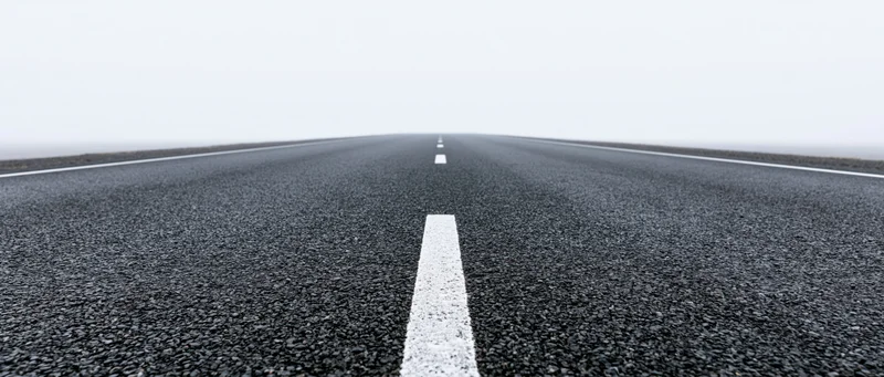 Straight asphalt road with white dashed center line receding into foggy horizon