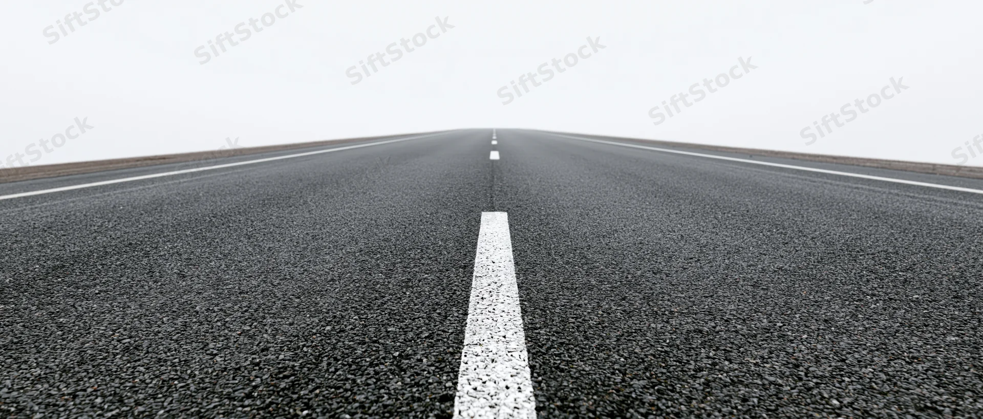 Straight asphalt road with white dashed centerline stretching toward horizon under overcast sky