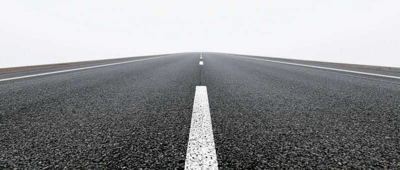 Straight asphalt road with white dashed centerline stretching toward horizon under overcast sky