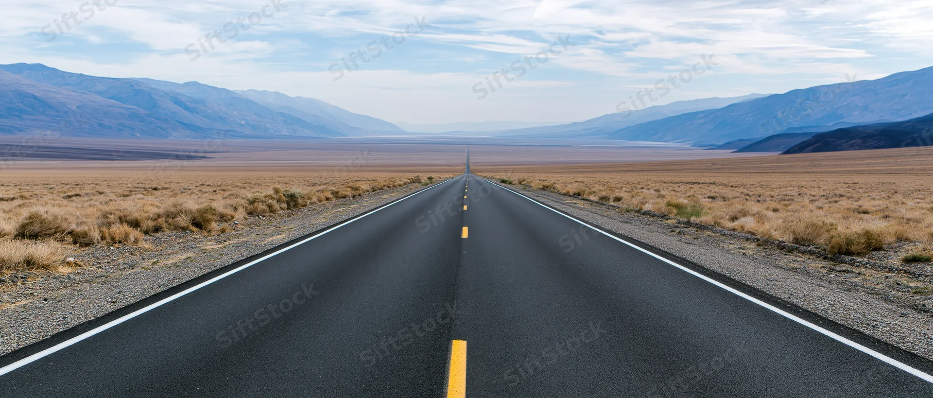 Straight asphalt highway stretching through arid desert landscape toward distant mountains under cloudy sky