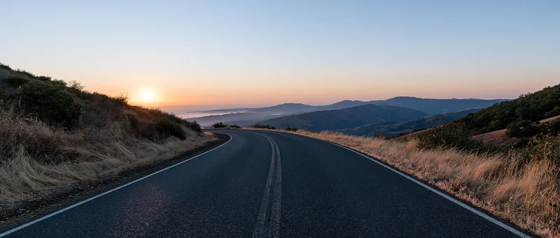 Winding asphalt road curving through mountain landscape toward sunset horizon