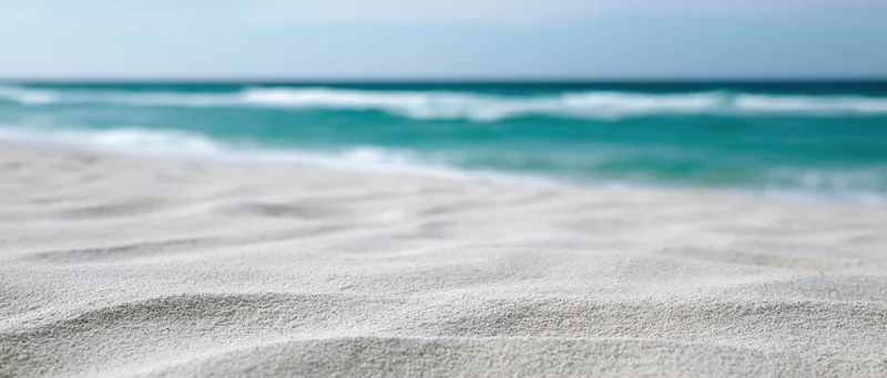 Close-up of rippled white sand on a beach with turquoise ocean waves in the background
